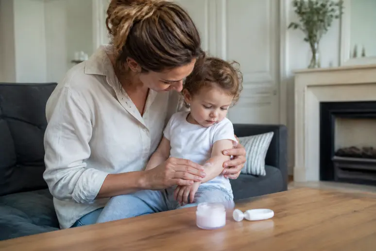 Mère appliquant avec douceur une crème anti démangeaison peau sur le bras d'un jeune enfant.