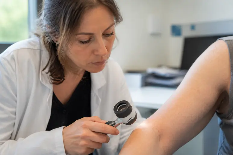 Professionnelle de santé examinant des taches rouges sur la peau d'une patiente avec un dermatoscope.