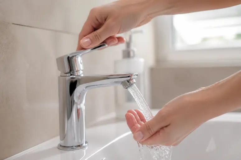 Mains faisant couler de l'eau claire au robinet d'un lavabo moderne