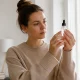 Une femme en pull beige tient un flacon pour savoir comment obtenir glass skin chez elle