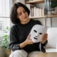 Une femme tient délicatement un masque Current Body rides dans son salon lumineux à Paris.
