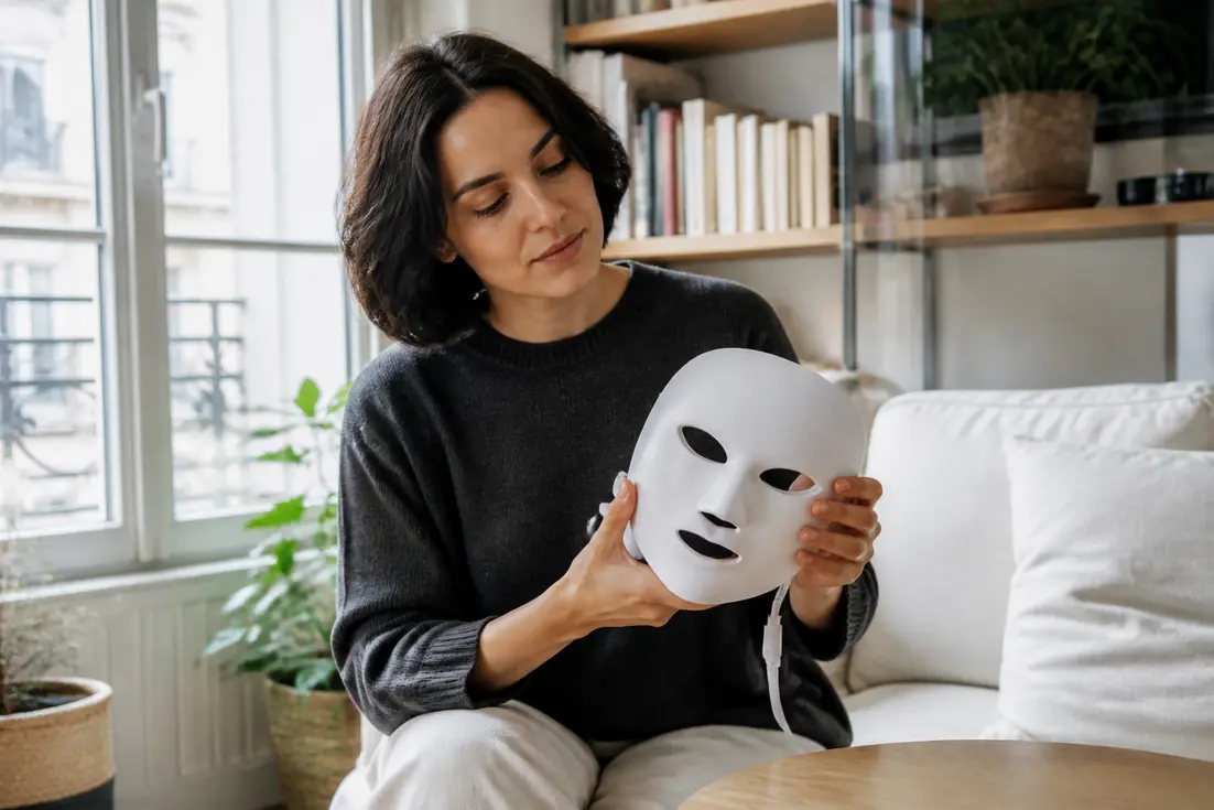 Une femme tient délicatement un masque Current Body rides dans son salon lumineux à Paris.