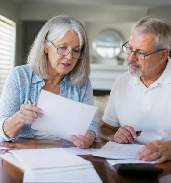 Un couple de seniors examine des documents administratifs pour choisir une mutuelle après 60 ans à domicile.