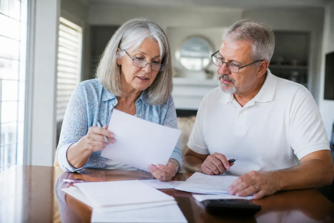 Un couple de seniors examine des documents administratifs pour choisir une mutuelle après 60 ans à domicile.